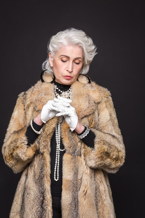 Senior rich woman posing with white gloves on isolated on black background. Serious lady looking at her hands.