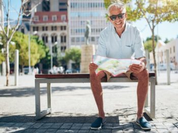 Happy senior male sitting on bench with a city map