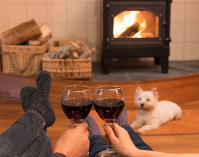Cosy couple by the fire with red wine and a west highland terrier westie dog.