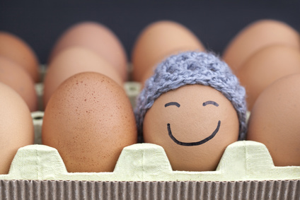 Smiling egg wearing a knitted hat souronded by blank brown eggs