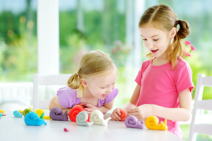 Two cute little sisters having fun together with colorful modeling clay at a daycare