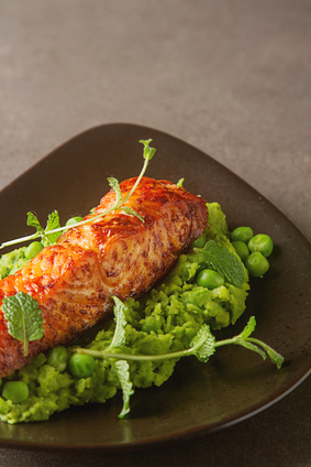 Grilled salmon pea puree decorated with mint on a brown plate. Gray background.