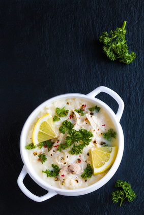Avgolemono, chicken soup with egg-lemon sauce, rice and fresh parsley leaves in white bowl on black stone background. Top view.