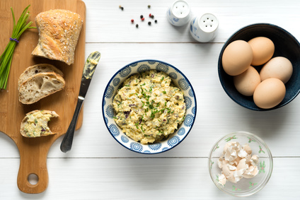 Homemade egg salad spread with mayonnaise, mustard, red onion sprinkled with chives, top view background on white table.