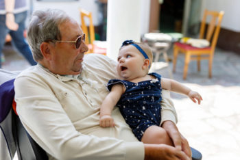 Cute little baby girl with grandfather on summer day in garden