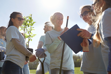 volunteering, charity, people and ecology concept - group of happy volunteers with tree seedlings and clipboard in park