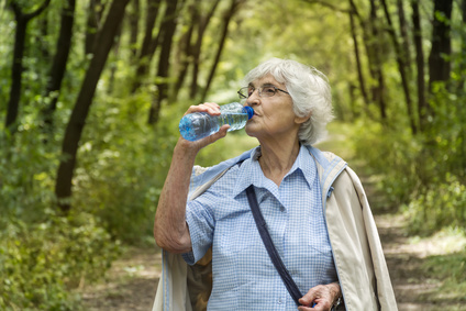 senior woman drinking water in the green summer park.Healthy living concept