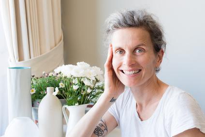 Middle aged woman with grey hair at table with flowers looking at camera and smiling (selective focus)