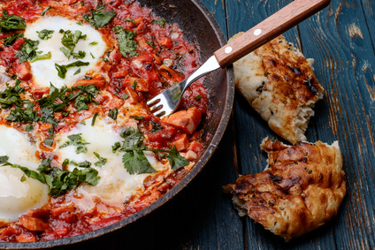 Fried eggs in a frying pan with tomatoes, sausage and greens.