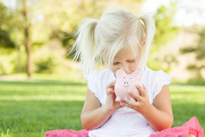 Cute Little Girl Having Fun with Her Piggy Bank Outside on the Grass.