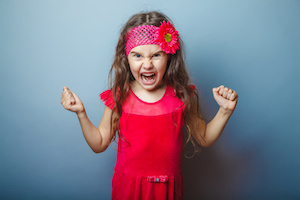 Girl European appearance haired child of seven in red bright dress on a gray background shouts, anger, anger