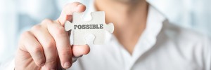 Businessman holding puzzle piece with Possible text in a conceptual image for positive attitude in resolving challenges and problems, close up horizontal banner format of his hand.