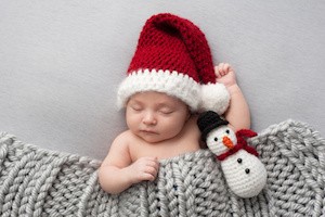 Sleeping, two week old, newborn, baby boy wearing a crocheted Santa hat with snowman plush toy.