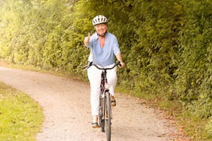 Fit healthy senior lady out cycling on her bicycle on a country road wearing a protective helmet and smiling happily at the camera in a healthy lifestyle concept
