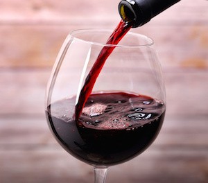 Pouring red luxury wine into glass and wooden background