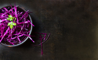 Shredded red cabbage in clay bowl on black background. Vegetarian healthy food. Top view