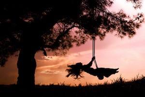silhouette of happy young woman on a swing with sunset background