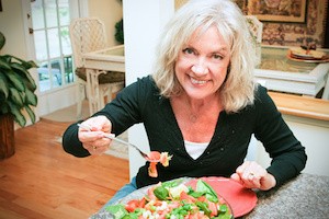 Fit, sexy senior woman eating a tossed green salad in her lovely modern home.