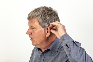 mature man puts hearing aid in the ear