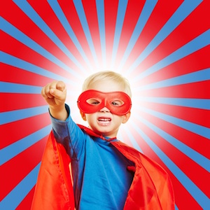 Kind als Superheld verkleidet mit geballter Faust vor einem Strahlen-Hintergrund