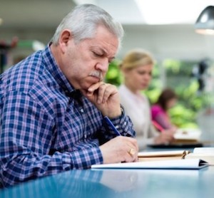 Senior man studying among young people in library