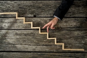 Businessman or student walking his fingers up wooden steps resembling a staircase mounted in rustic wooden boards in a conceptual image of personal and career development, success and aspiration.