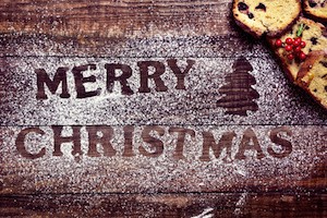 high-angle shot of a wooden table sprinkled with icing sugar where you can read the text merry christmas, and some pieces of fruitcake
