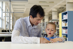 Child pupil with parent or teacher reading a book in public library.