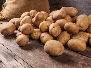 Pile of potatoes lying on wooden boards with a potato bag in the background