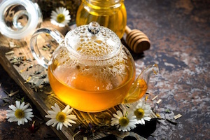 fragrant chamomile tea in a glass teapot on dark background, horizontal