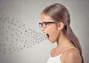 Side view portrait angry child screaming, alphabet letters coming out of her mouth, isolated grey wall background. Negative human face expressions, emotion, reaction. Conflict, confrontation concept