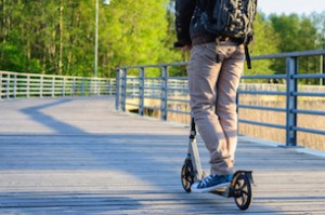 Young man in casual wear on kick scooter in park at sunset