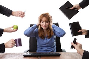 overwhelmed business woman sitting at her desk surrounded by many male hands holding different objects