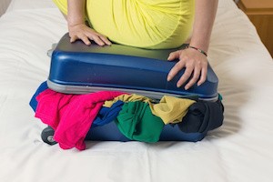 Young woman try to close the overfilled suitcase in the room.