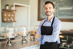 Portrait of a young business owner wearing an apron and standing in front of his cake shop