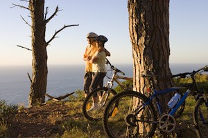 Mature couple mountain biking on clifftop trail, looking at Atlantic Ocean horizon, side view
